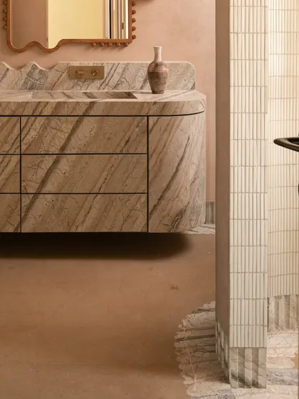 We call this bathroom a 'chic desert dream'. It features blush-toned micro-concrete walls and a monolithic vanity carved from veined Corteccia marble. The stone appears to trickle down onto the floor, creating a fluted skirting detail that is both organic and luxurious.