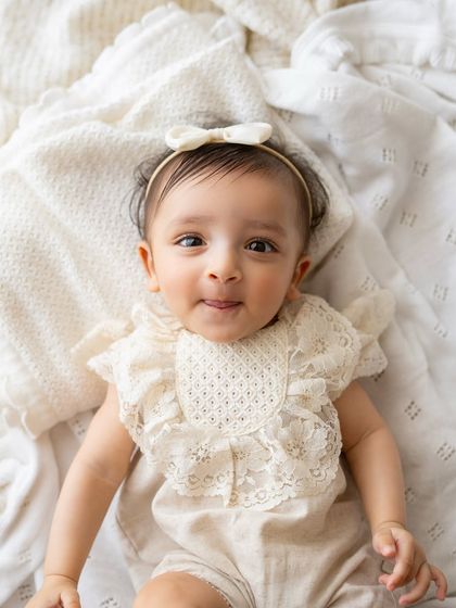 A close-up portrait of a 6-month-old baby girl. The delicate lace romper and her sweet expression make this a timeless image.