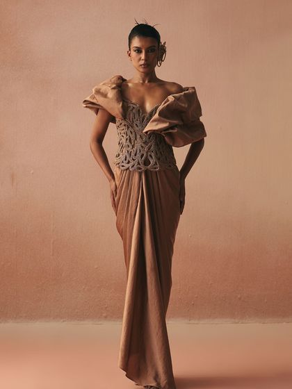 This draped gown features dramatic, structured puff sleeves that create a powerful shoulder line. The cord-embroidered bodice and flowing skirt balance structure and fluidity.