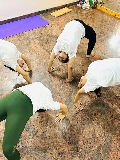 Students working together in a circle to practice Chakrasana, or Wheel Pose. This shows the supportive and collaborative atmosphere we cultivate in the studio.