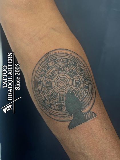 A detailed tattoo of the Konark Sun Temple wheel with a silhouette of Buddha, blending two distinct spiritual traditions.