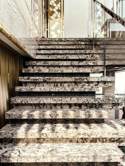 The exterior staircase of the "House Reversed" in Hassan. The treads are made of a unique granite, and the glass and brass railing adds a touch of modern luxury to the entrance.