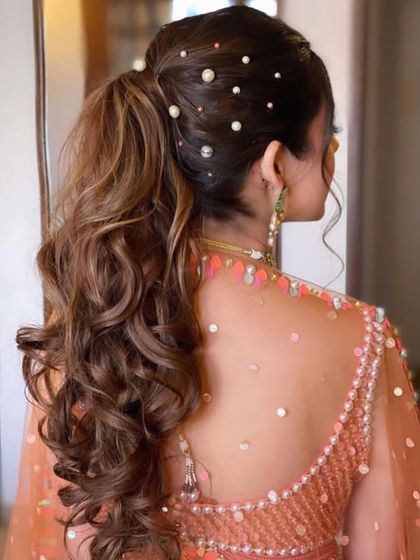 A chic and modern ponytail for a Roka ceremony. The hair is styled with volume at the crown and soft curls, with pearl accessories scattered throughout for a touch of elegance.