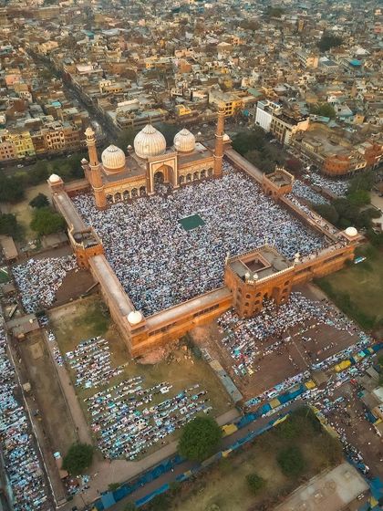 This drone shot captures an angled view of the Jama Masjid courtyard, showing the scale of the Eid prayer gathering. The perspective highlights both the architectural grandeur and the immense number of people present.