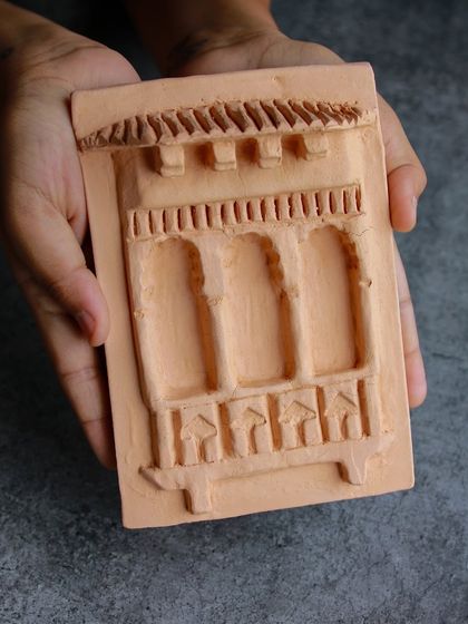 A student holds up their architectural relief tile, inspired by the design of a traditional Indian jharokha or window.