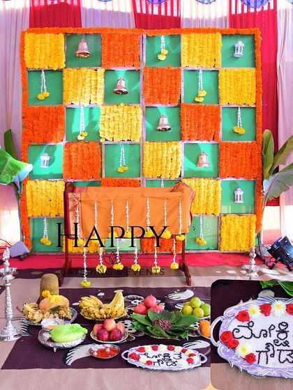 A complete traditional setup for an Annaprasanna ceremony. The decor includes a marigold backdrop, a low seating arrangement, and a spread of ceremonial food items.