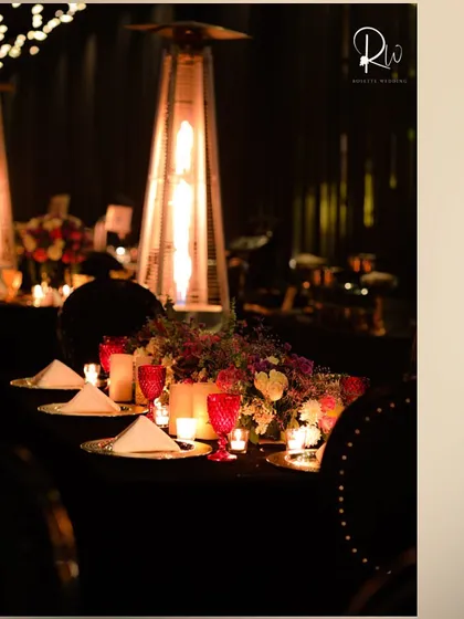 A tablescape for a winter cocktail event, with a patio heater providing warmth and ambiance. The red glassware adds a pop of color to the dark setting.