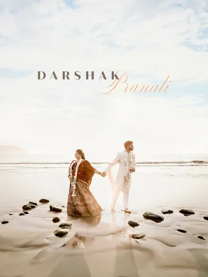 A breathtaking destination wedding portrait on the beach. The couple holds hands against a vast ocean and a beautiful sky, creating a truly epic and romantic memory of their special day.