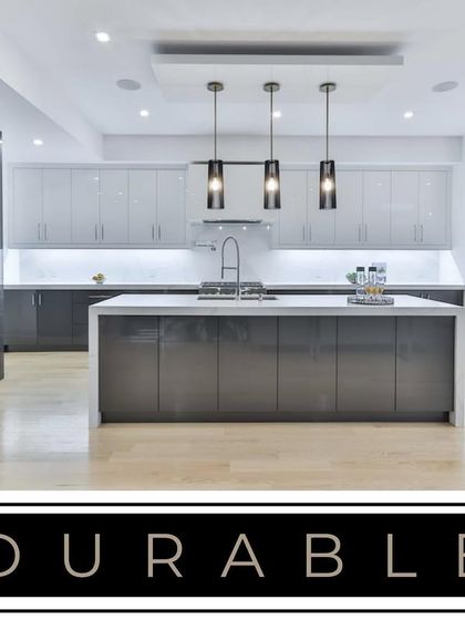 This spacious kitchen showcases a two-tone grey high-gloss finish with an island. The design incorporates integrated ovens and handle-less cabinets, emphasizing a durable and sleek aesthetic built for modern living.