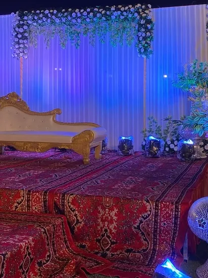 A simple yet elegant Sangeet stage, featuring a white drape backdrop with blue uplighting, a classic chaise lounge, and large silver-mirrored vases.