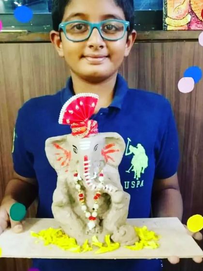 A young student with glasses smiles as he displays the Ganpati idol he created, a perfect example of the creativity nurtured in our classes.