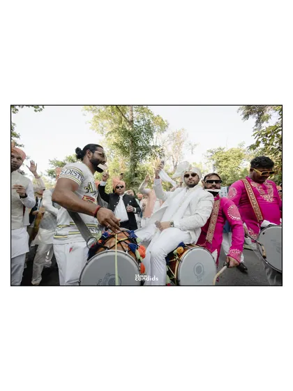 The groom makes a grand entrance, sitting on a dhol, surrounded by his energetic friends. This shot is pure baraat energy and joy.