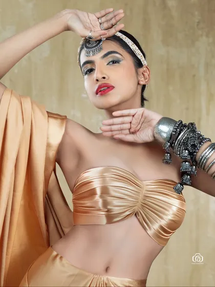 A creative studio portrait with a golden satin outfit and traditional silver jewelry. The contrast between the warm gold fabric and the cool silver accessories creates a visually interesting fusion look.