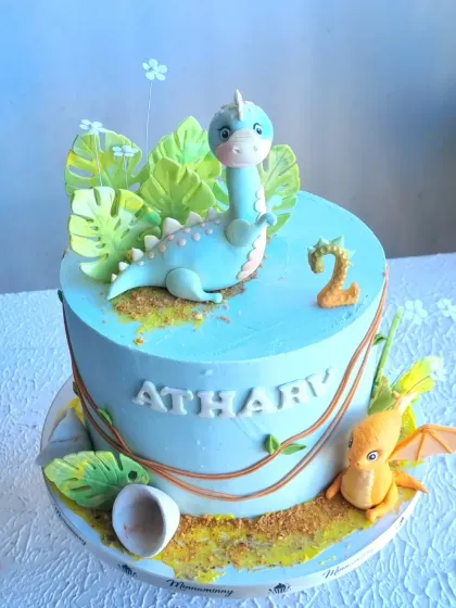 A different angle of the dinosaur cake, showing the placement of the fondant leaves and the number two topper.