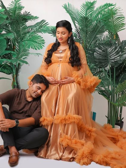 A tender moment between a couple in our studio. The father-to-be rests his head on the baby bump, surrounded by lush greenery props and the mother's stunning golden gown.