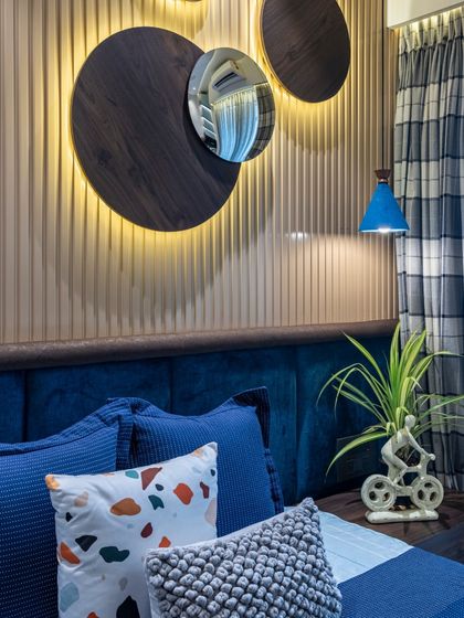 This bedroom in the Filigree House features a deep blue velvet headboard and matching accents. The circular wall decor with integrated lighting adds a modern, artistic touch to the serene space.