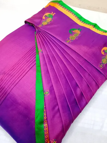 A purple cotton-silk saree with peacock embroidery, pleated for a special occasion.