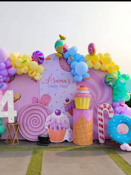 A delightful Candyland setup for a 4th birthday, featuring a backdrop of giant candies, a light-up number '4', and props like cupcakes, donuts, and a candy cane.