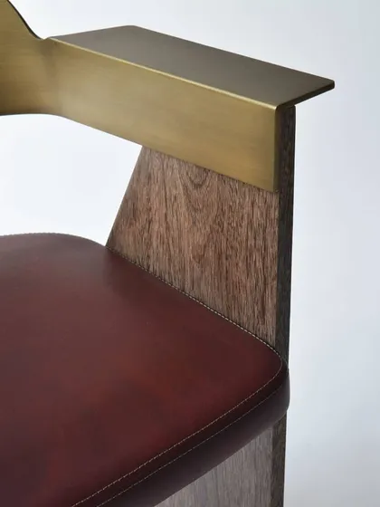 A close-up of the AERO chair reveals our commitment to material fusion. The design features a sharp, dynamic frame of Sucupira wood, an armrest crafted from a single piece of antique bronze, and a seat upholstered in rich, hand-stitched leather.