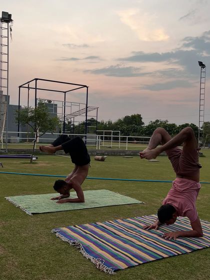 This image captures two practitioners in advanced arm balances, a forearm stand (Pincha Mayurasana) and a side crow variation, showcasing incredible strength and control.