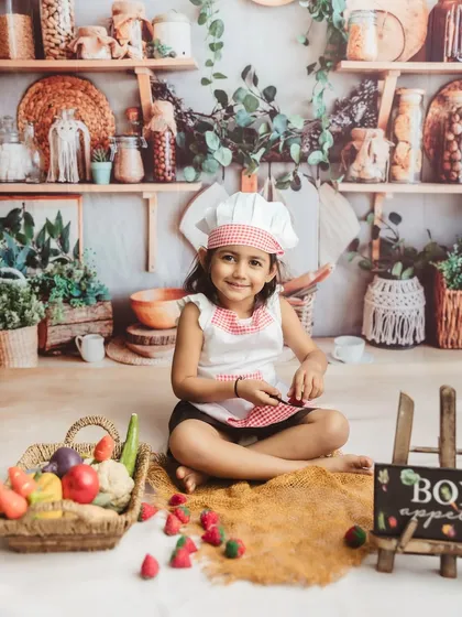 A sweet smile from our little chef, surrounded by a basket of colorful play vegetables.
