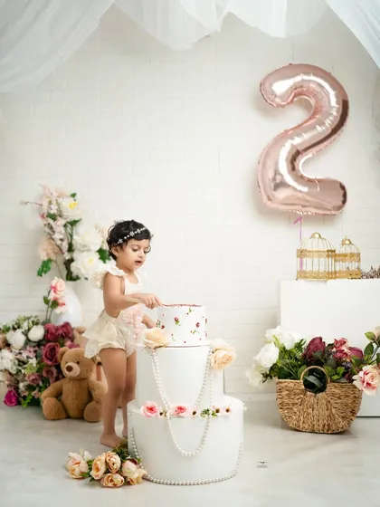 A little princess reaches for her second birthday cake. The setup includes soft florals, teddy bears, and a beautiful two-tiered cake to mark the special occasion.