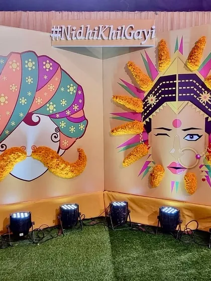 A fun and personalized photo booth for a Mehendi night. The backdrop features quirky illustrations and the couple's hashtag, with marigold details adding a traditional touch.