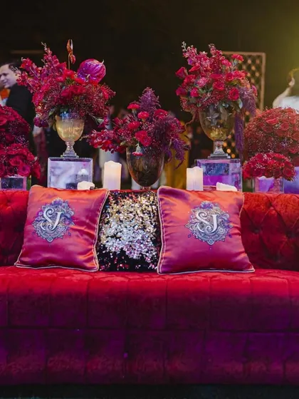 A plush red velvet sofa with custom-monogrammed cushions, creating a regal photo-op for the couple.
