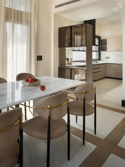 Where design and dining intersect. This dining area exudes quiet luxury, with a marble table, plush seating with golden details, and an adjacent open kitchen with a minimalist aesthetic.