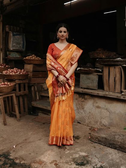 A powerful full-length portrait of a woman in a vibrant saree standing confidently in a rustic Varanasi market, blending grace with a strong presence.