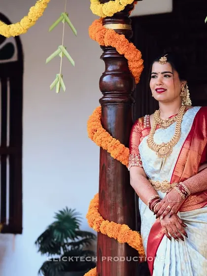A full-length portrait of a bride standing by a traditionally decorated pillar, looking serene and beautiful.