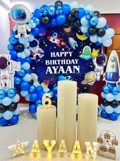A fantastic outer space adventure for a 6th birthday. This setup includes a planet-filled backdrop, an astronaut cutout, a rocket ship, and a blue and black balloon arch, ready for blast-off.