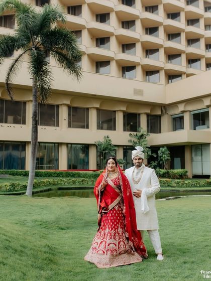 A grand portrait of the couple in the lush green lawns of the JW Marriott Juhu, with the iconic hotel in the background.