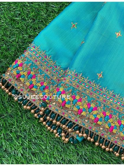 A close-up of the sleeve border on the turquoise blouse. The intricate pattern uses pink, yellow, and blue thread, with a fringe of dark green and gold beads.