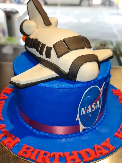 An out-of-this-world 3D sculpted cake for a future astronaut. This NASA space shuttle cake is crafted with smooth blue fondant and a detailed, edible shuttle, showcasing my skill in creating unique, three-dimensional designs.