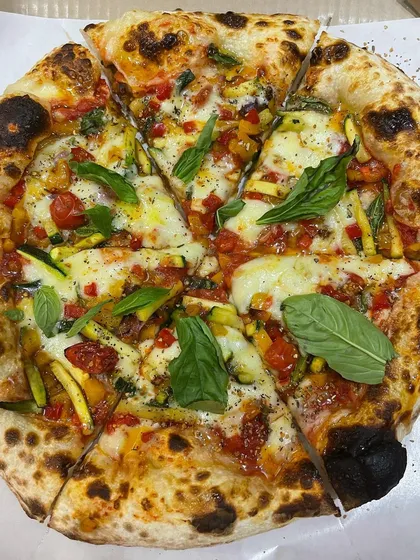 A vibrant and healthy veggie pizza. This one is loaded with fresh zucchini, colorful bell peppers, cherry tomatoes, and basil, showing that a vegetable pizza can be incredibly delicious.