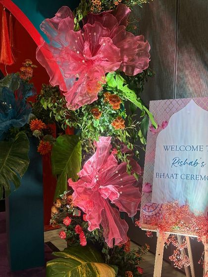 The welcome sign for Rishab's Bhaat ceremony, framed by large, whimsical pink and blue fabric flowers. This detail shows how the artistic and colorful theme was carried through every element of the event.