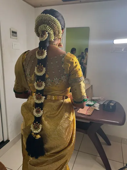 A view of Vani's traditional bridal hairstyle from the back. The long braid is adorned with jasmine flowers and a full set of jadai billai, completing her classic Muhurtham look.