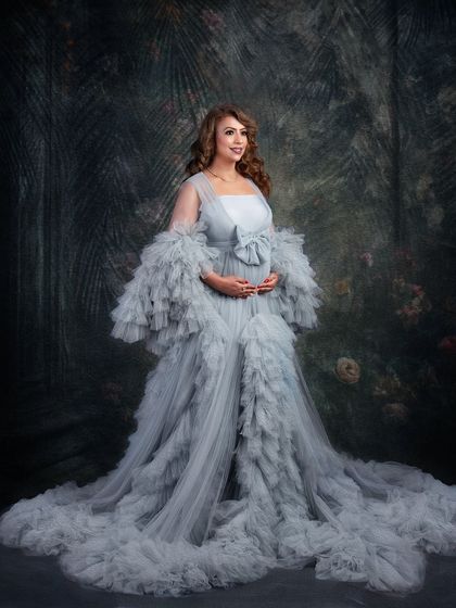 A full-length view of the magnificent grey ruffled gown. The sheer volume and texture of the dress make for a dramatic and high-fashion maternity statement piece.