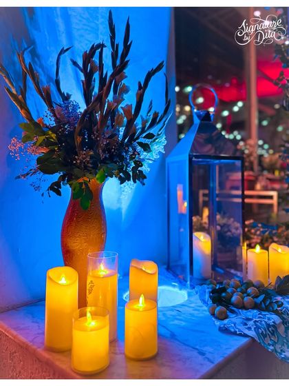 An arrangement of flameless pillar candles and a tall floral vase, bathed in blue light to create a moody, evening atmosphere.