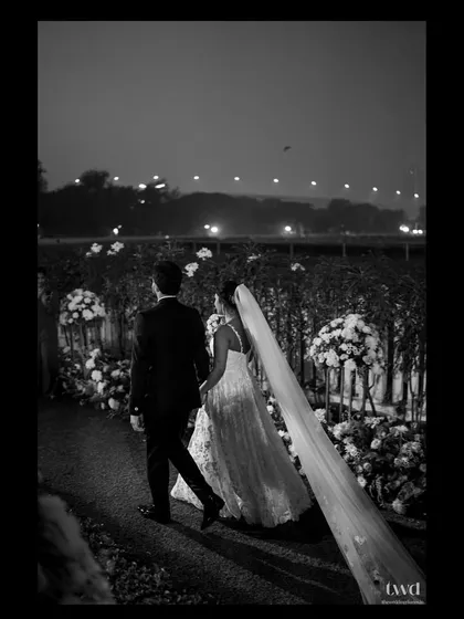A timeless black and white photograph of the newly married couple walking through the floral-lined path at their venue. This quiet, reflective moment captures the beginning of their journey as husband and wife.