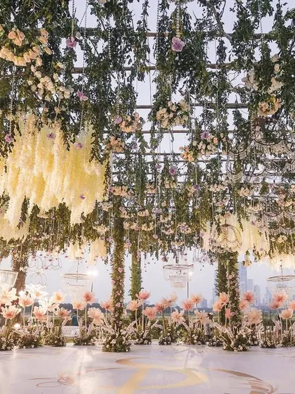 A beautiful reception dance floor under a ceiling of hanging greenery and pastel florals. The design creates a magical, open-air ballroom feel with the city skyline in the distance.