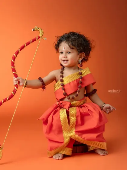 A smiling little Lord Ram, holding his bow with confidence. The warm, gradient orange background provides a simple yet powerful setting for this portrait.