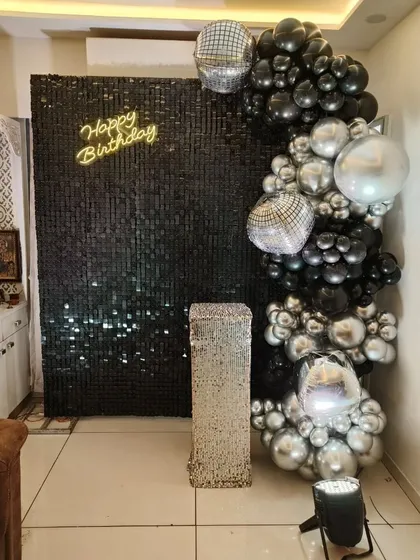 A chic and modern party corner with a black sequin wall. The balloon arch with black, silver, and disco ball accents, along with a neon 'Happy Birthday' sign, is perfect for a stylish office celebration.