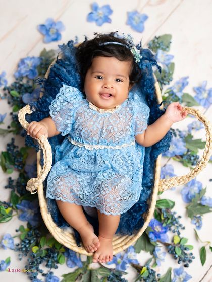 Our little "Blueberry" girl, looking adorable in a blue lace dress. This overhead shot in a basket surrounded by blue flowers is a beautiful way to celebrate a 100-day milestone.