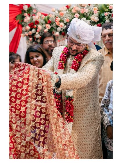 The groom participates in a wedding ritual, holding up the bride's ornate red dupatta. This image documents the important cultural traditions of the ceremony.