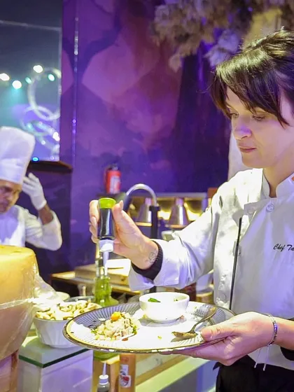 Chef Tatyana, one of our international chefs, artfully drizzles a finishing sauce onto a plate of risotto, showcasing her expertise and attention to detail.