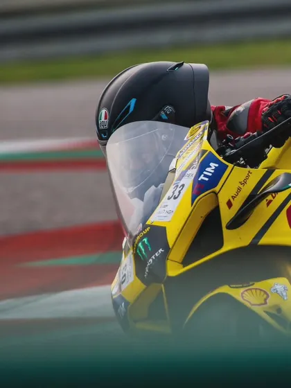 A close up shot focusing on the helmet and front fairing of a yellow Ducati race bike at speed. The details of the sponsors like Givi and Audi Sport are clearly visible.