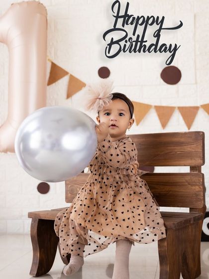 Holding a silver balloon, this little one is the star of her first birthday shoot. The simple setup with a 'Happy Birthday' sign keeps the focus on her.