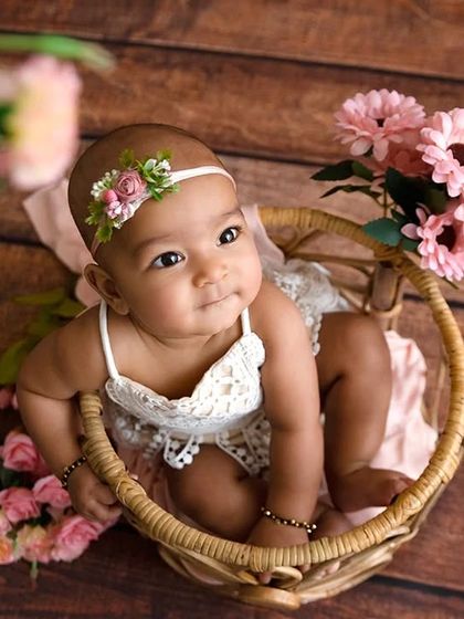 A high-angle shot of a baby girl in a wicker basket, framed by pink flowers.